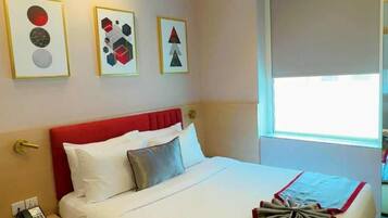 A hotel room with a bed, bedside table, and a window.