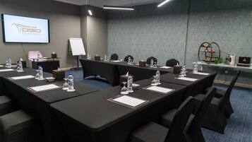 A conference room with long tables, chairs, water bottles, and a projector screen displaying 'VGO GRAND HOTEL'.