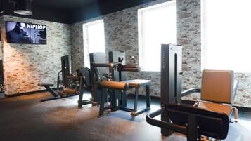 A gym with exercise equipment, a television displaying 'HIPHOP,' and large windows.