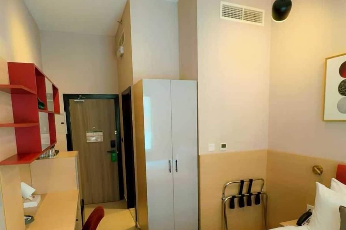 Una habitación de hotel con cama, escritorio, silla, armario y lámpara colgante.