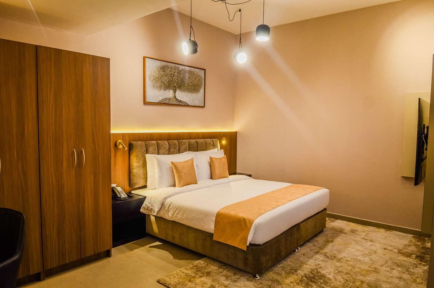 Habitación de hotel con una cama grande, armario de madera, mesita de noche con lámpara y un cuadro en la pared.