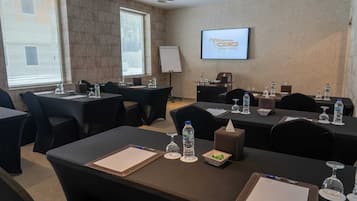 A conference room with tables, chairs, water bottles, and a screen displaying the Grand Hotel logo.