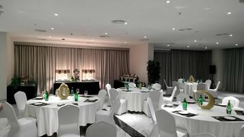 Une salle de conférence avec des tables rondes, des chaises blanches et une scène équipée d’un pupitre.