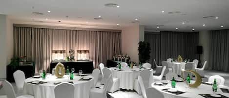 Un salón de conferencias con mesas redondas, sillas blancas y un escenario con un atril.