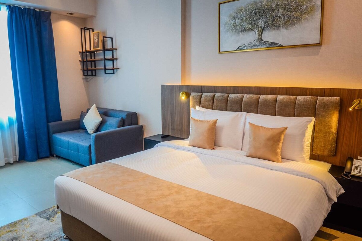A hotel room with a large bed, a sofa, a desk, and a painting on the wall.