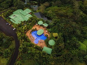 Vista aérea de un complejo turístico con piscina, edificios de techo verde y abundante vegetación.
