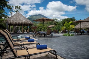 A resort with thatched-roof structures, lounge chairs, and umbrellas. - Arenal Manoa Resort And Hot Springs (La Fortuna)