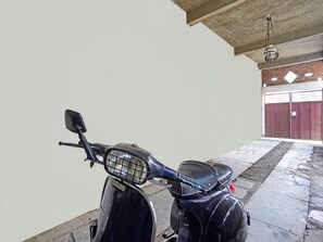 A scooter parked in a garage with a concrete ceiling and a brick wall. - Spot On 91672 House Of Henny Tea (Jember)