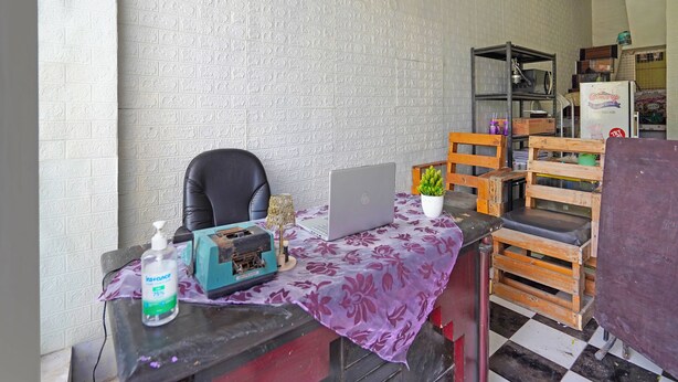 Una habitación con pared de ladrillo, una laptop sobre una mesa, una silla, una planta pequeña y un banco de madera.