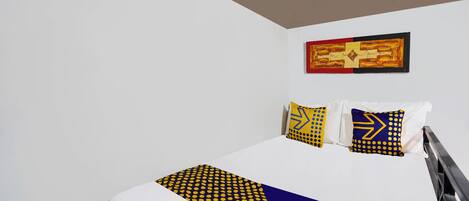 A hotel room with a bed, white walls, and a framed artwork above the bed.