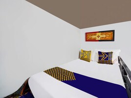 Una habitación de hotel con cama, paredes blancas y una obra de arte enmarcada sobre la cama.