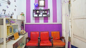 Una habitación con paredes a rayas moradas y blancas, un armario de madera con diversos objetos, y tres sillas de cuero rojo.