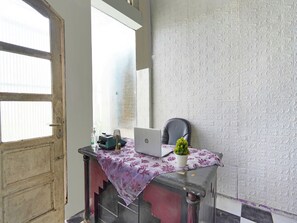 A room with a wooden door, a window, a laptop on a table, a chair, and a patterned wall. - Spot On 91672 House Of Henny Tea (Jember)