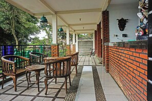 A covered outdoor seating area with wooden furniture, a brick wall, and a decorative headpiece on the wall.