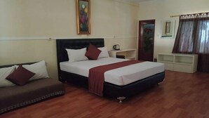 A hotel room with a bed, a sofa, a painting on the wall, a coffee table, and a window with curtains.