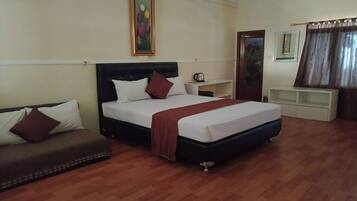 Quarto de hotel com uma cama, sofá, quadro na parede, mesa de centro e janela com cortinas.
