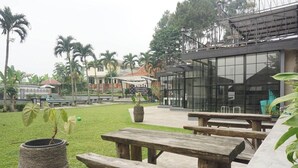 A courtyard with wooden picnic tables, a stone planter, and a modern building with large windows. - Cunang Hill Hotel & Resort by Zuzu (Cilobak)
