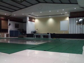 A spacious indoor area with a stage, a whiteboard, and a green carpeted floor.