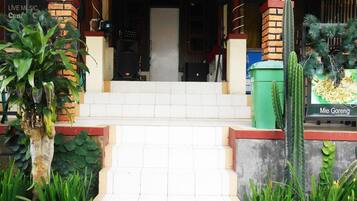 Entrada de um edifício com degraus que levam a uma porta, cercada por plantas e um letreiro do 'd Cunang Caffe & Resto'.