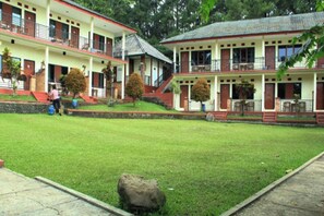 A two-story building with a flat roof, a central courtyard, and a person walking in the distance. - Cunang Hill Hotel & Resort by Zuzu (Cilobak)