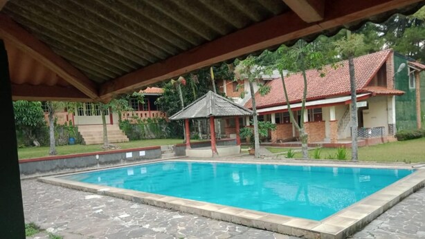A swimming pool with a stone deck, a gazebo, and a house with a red roof in the background.