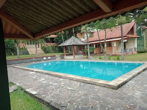 A swimming pool with a stone deck, a gazebo, and a house with a red roof in the background.