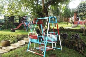 A playground with swings and slides, surrounded by greenery and a building in the background. - Cunang Hill Hotel & Resort by Zuzu (Cilobak)