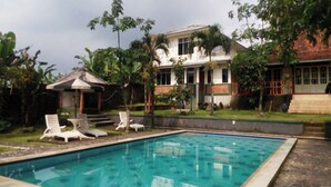 A swimming pool with lounge chairs, a gazebo, and a house with a tiled roof. - Cunang Hill Hotel & Resort by Zuzu (Cilobak)