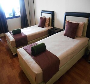 Two single beds with headboards, a nightstand, and a window with curtains.