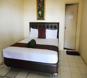 A hotel room with a bed, a painting, a door, and a tiled floor. - Cunang Hill Hotel & Resort by Zuzu (Cilobak)