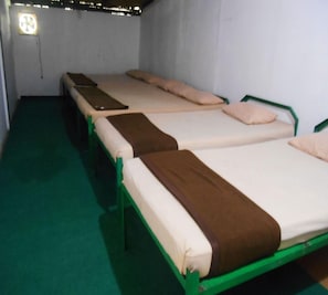A row of bunk beds with green frames and white mattresses, a green carpeted floor, and a wall-mounted light fixture.