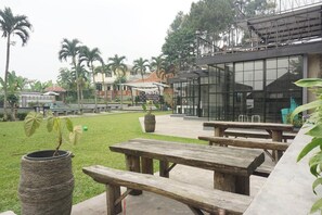 Un patio con mesas de picnic de madera, una jardinera de piedra y un edificio moderno con ventanas grandes.