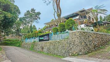Um muro de pedra com uma placa indicando o hotel 'Cang HOLL', uma estrada sinuosa e uma árvore grande.