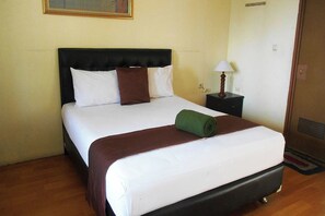 Una cama bien hecha, con cabecera negra, almohadas blancas y marrones, y una toalla verde.