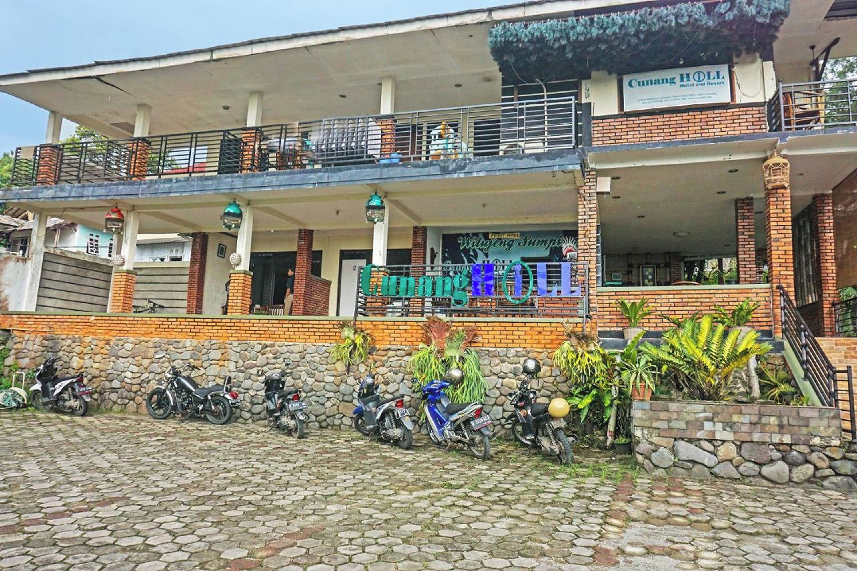 A hotel with a covered outdoor area, a signboard, and several motorcycles parked in front.