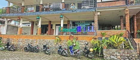 A hotel with a covered outdoor area, a signboard, and several motorcycles parked in front.