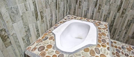Un baño con piso de mosaico de piedra, inodoro blanco y pared de piedra.