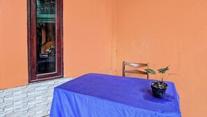 A table with a blue tablecloth, a chair, and a potted plant on a balcony with orange walls and a window. - Spot On 91771 Homestay Bang Haji (Praya)