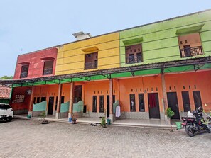 Ein mehrstöckiges Gebäude mit farbenfroher Fassade, mehreren Balkonen und einem überdachten Eingangsbereich, vor dem ein Motorrad steht.