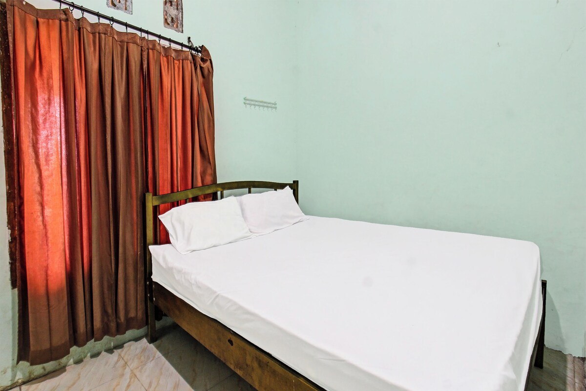 A single bed with white bedding in a room with a green wall and a brown curtain.