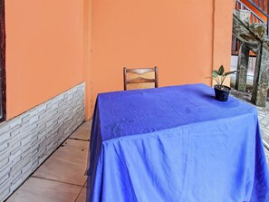 A table with a blue tablecloth, a wooden chair, and a potted plant on a balcony with orange walls and a tiled floor. - Spot On 91771 Homestay Bang Haji (Praya)