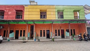 A colorful building with multiple doors and windows, a covered entrance area, and several potted plants. - Spot On 91771 Homestay Bang Haji (Praya)