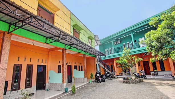 A courtyard with a covered walkway, potted plants, and parked motorcycles. - Spot On 91771 Homestay Bang Haji (Praya)