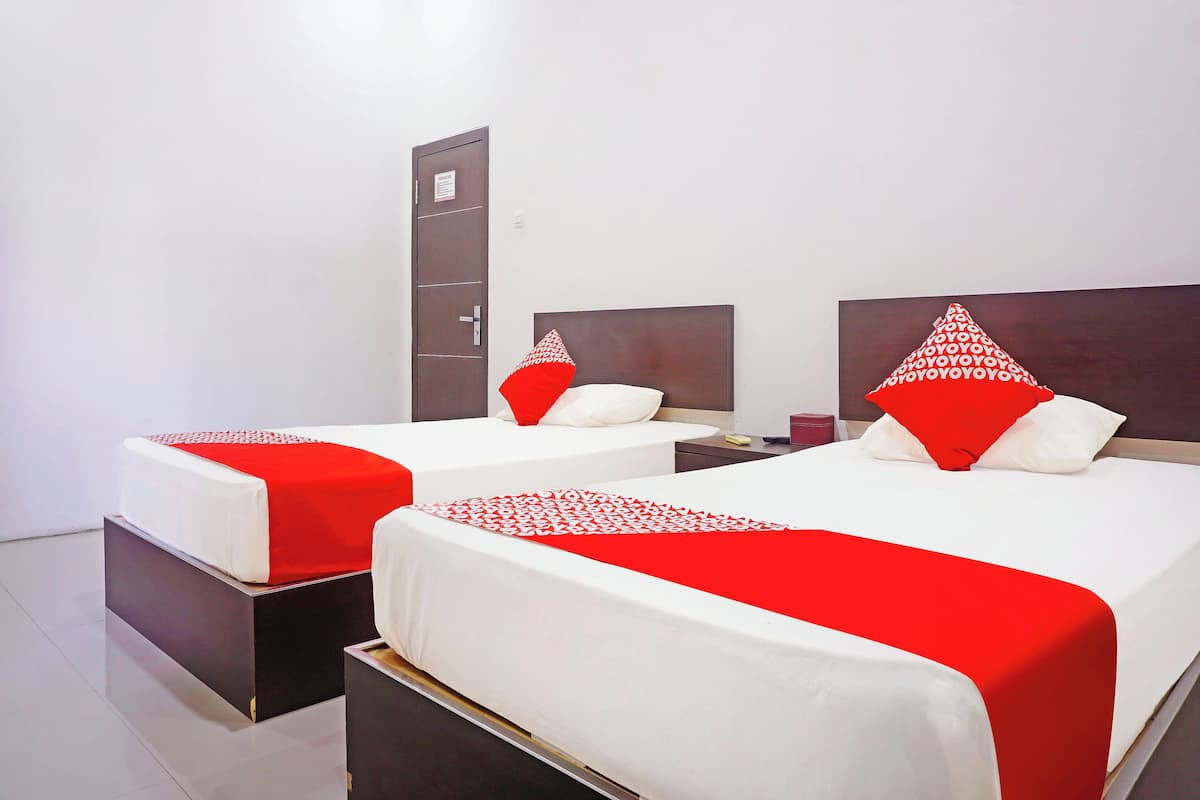Een hotelkamer met twee bedden, elk met een rode en witte spreideken, een houten hoofdbord en een nachtkastje met een rode doos.