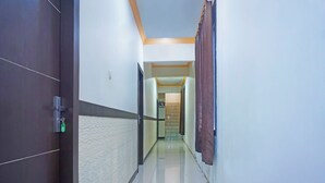 A hotel hallway with a dark door, a patterned wall, and a plain wall leading to a room. - Oyo 91432 Dalle 5151 Jeneponto (Tanjung Pinang)
