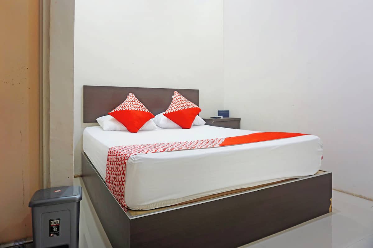 Een bed met een wit matras, twee rode kussens en een beddeken met een rood-wit patroon.