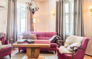 A room with a wooden table, a pink sofa, a chair with a fur throw, and a chandelier.