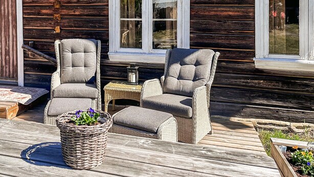 A wooden deck with two wicker chairs and a table, a potted plant, and a rustic building in the background. - Beautiful home in Bagn with WiFi (Bagn)