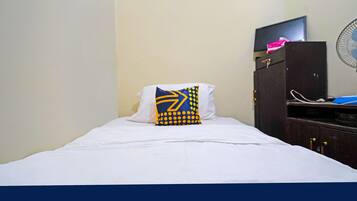 A single bed with a white sheet and a pillow with a geometric pattern. A television is mounted on a cabinet above the bed.