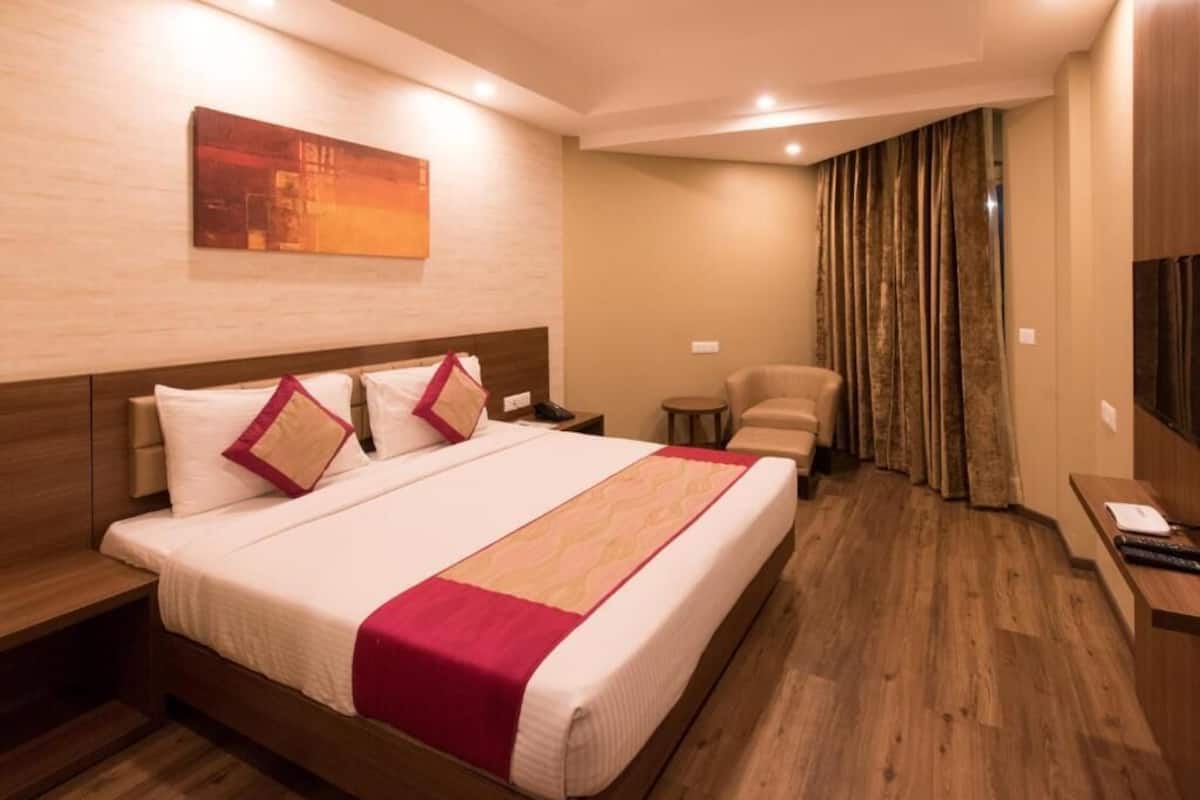 A hotel room with a large bed, a desk, a chair, a TV, and a painting on the wall.